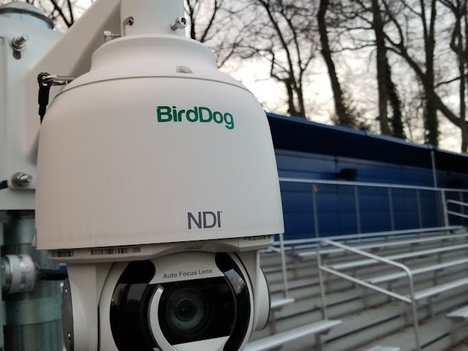 A BirdDog outdoor PTZ camera with NDI branding mounted at a stadium rail