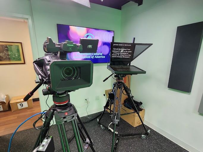 A camera and teleprompter aimed at a set inside the Karjian Hairenik Media Center studio.