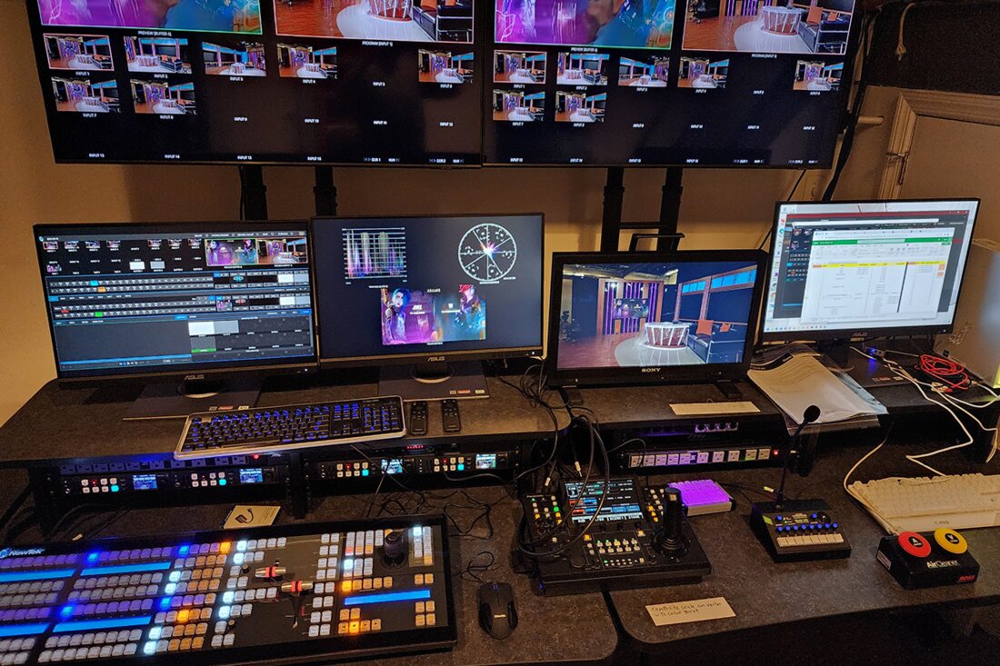 A broadcast control position with audio console, switcher surfaces, and multiviewer wall