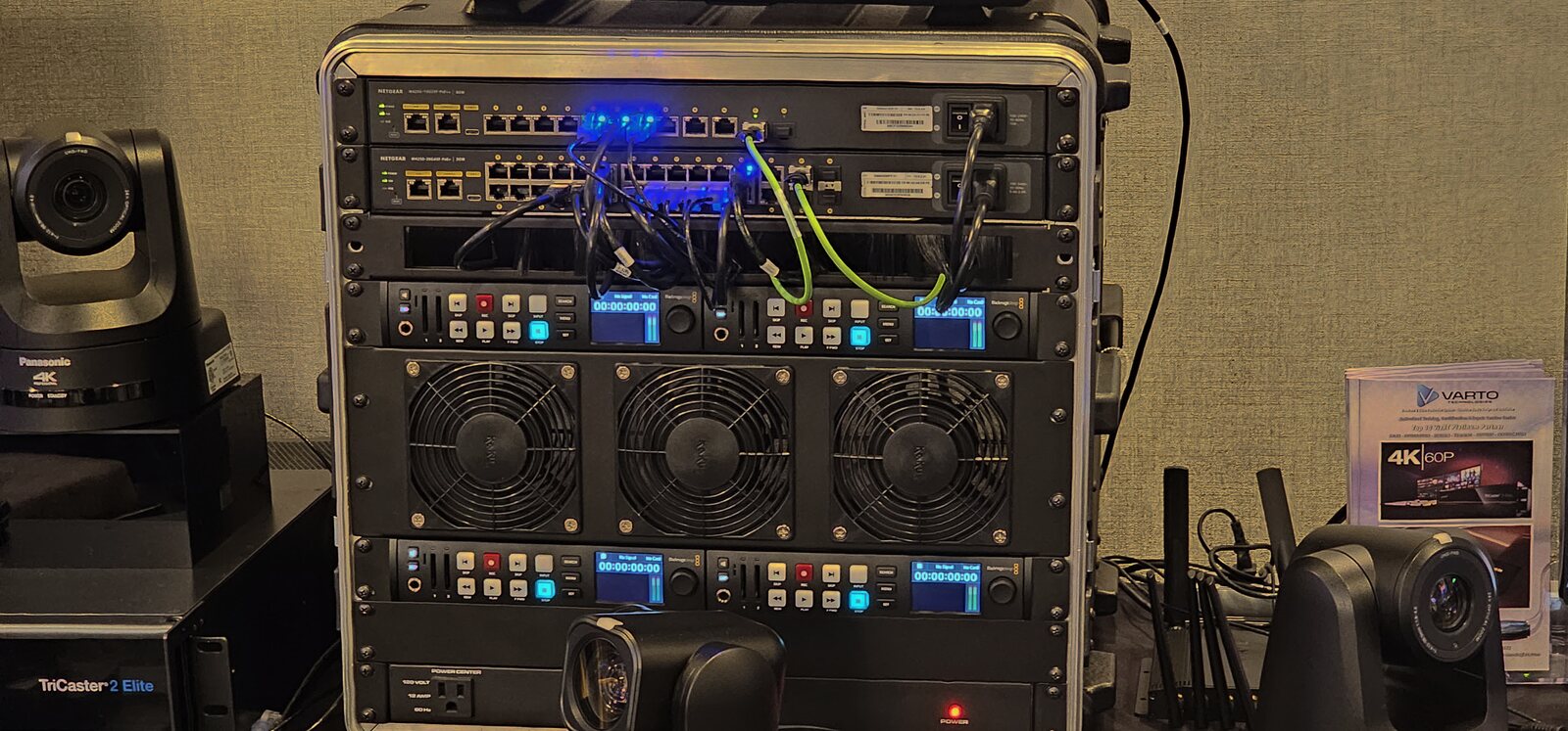 A production flypack rack with NETGEAR AV switches, a TriCaster and PTZ cameras staged at Varto