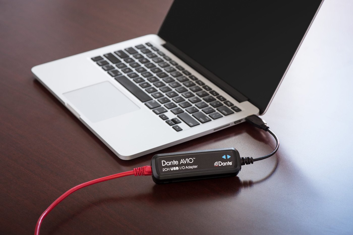 A Dante AVIO USB adapter connected to a laptop on a desk, its network cable running off the table