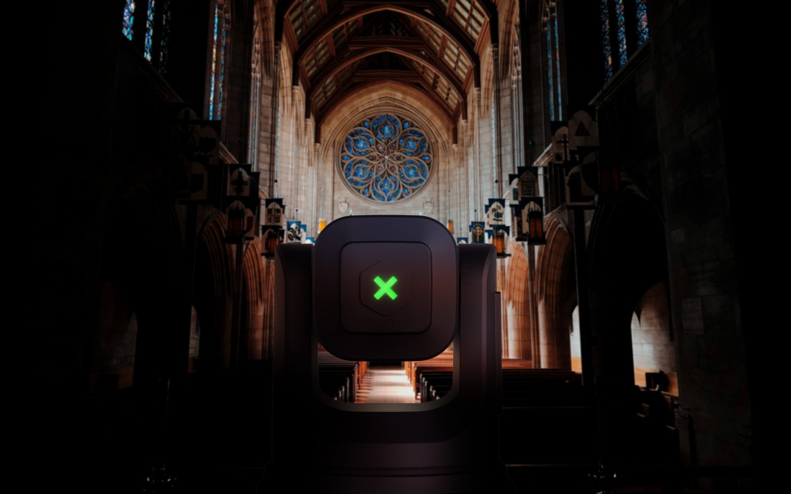 A black BirdDog X4E Ultra PTZ camera seen from behind in the aisle of a dim church, facing the altar