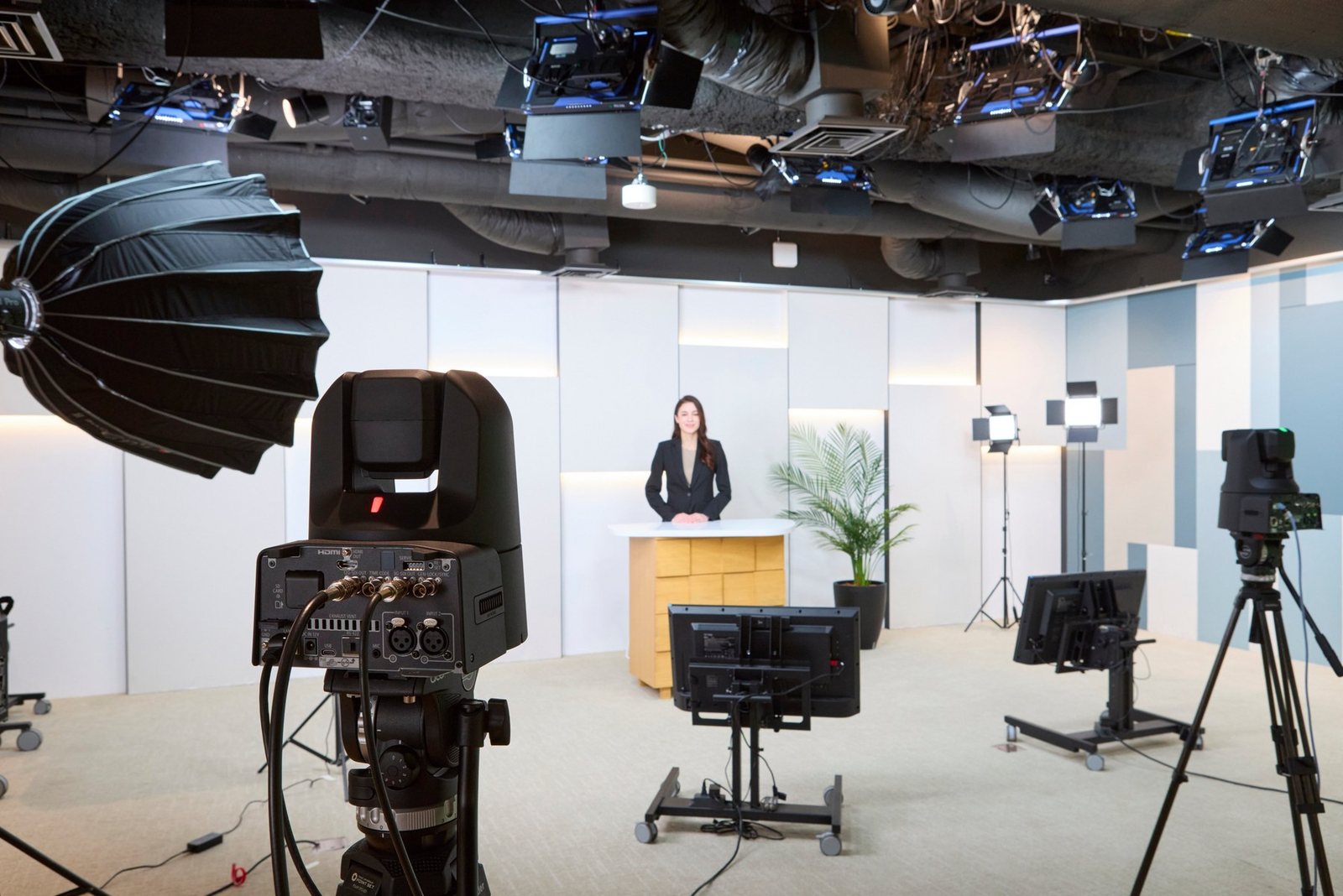 Black Canon PTZ camera on a tripod in the foreground of a news studio, a presenter at the desk behind it