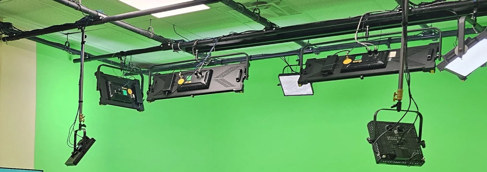 Lighting grid over a green cyclorama, with black LED panels, a Fresnel and blue network cables hung from the pipes