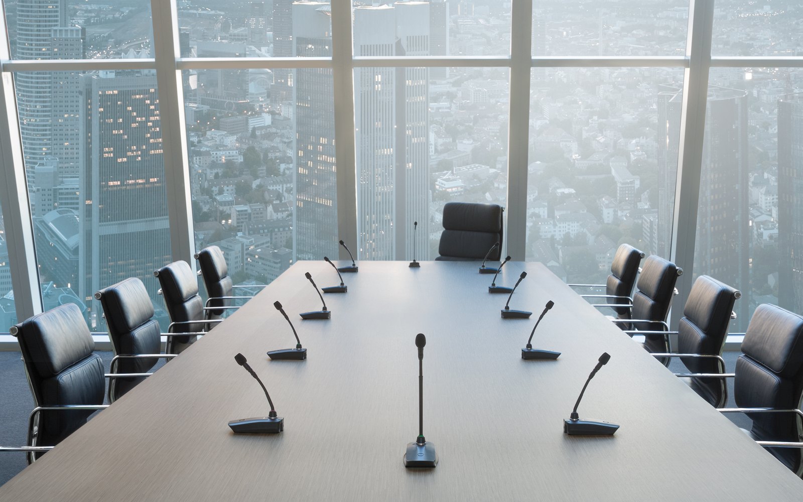 An empty boardroom with a Shure gooseneck microphone at each seat along a long table