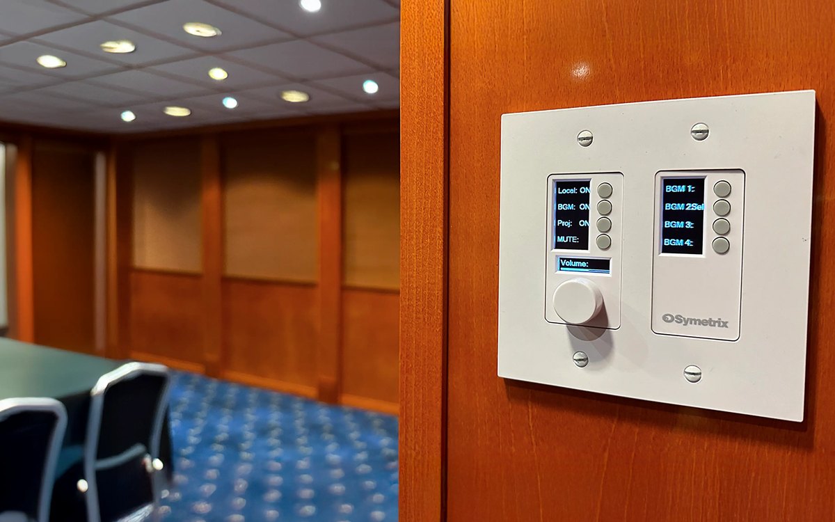 A white Symetrix two-gang wall controller with a knob, eight buttons and two displays beside a boardroom door
