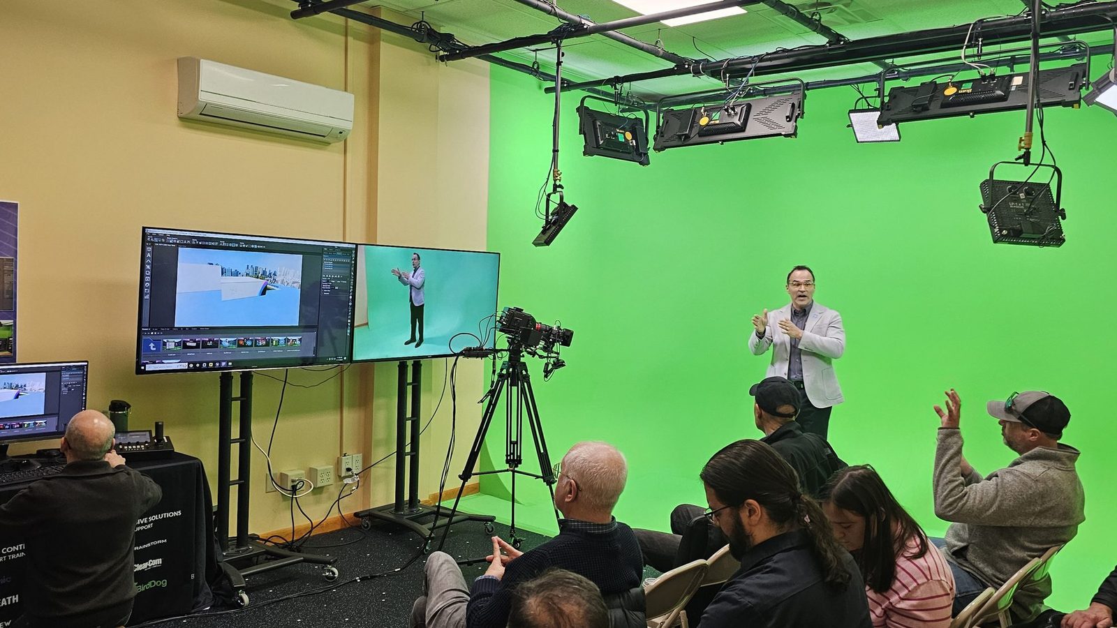 A presenter on the green cyclorama while monitors show the virtual set and the keyed shot, with an audience watching