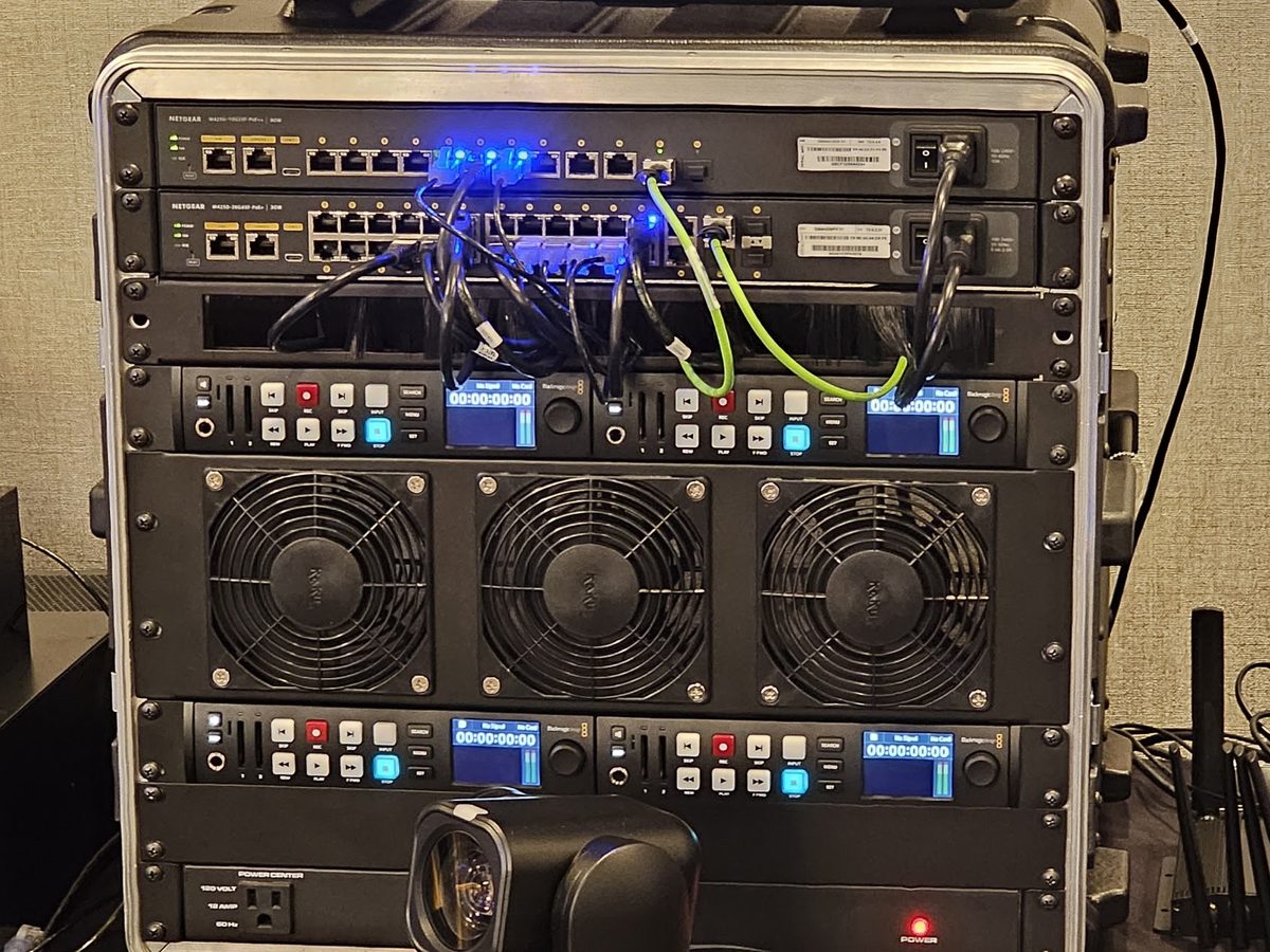 Managed NETGEAR AV switches racked above production hardware, with PTZ cameras beside the rack
