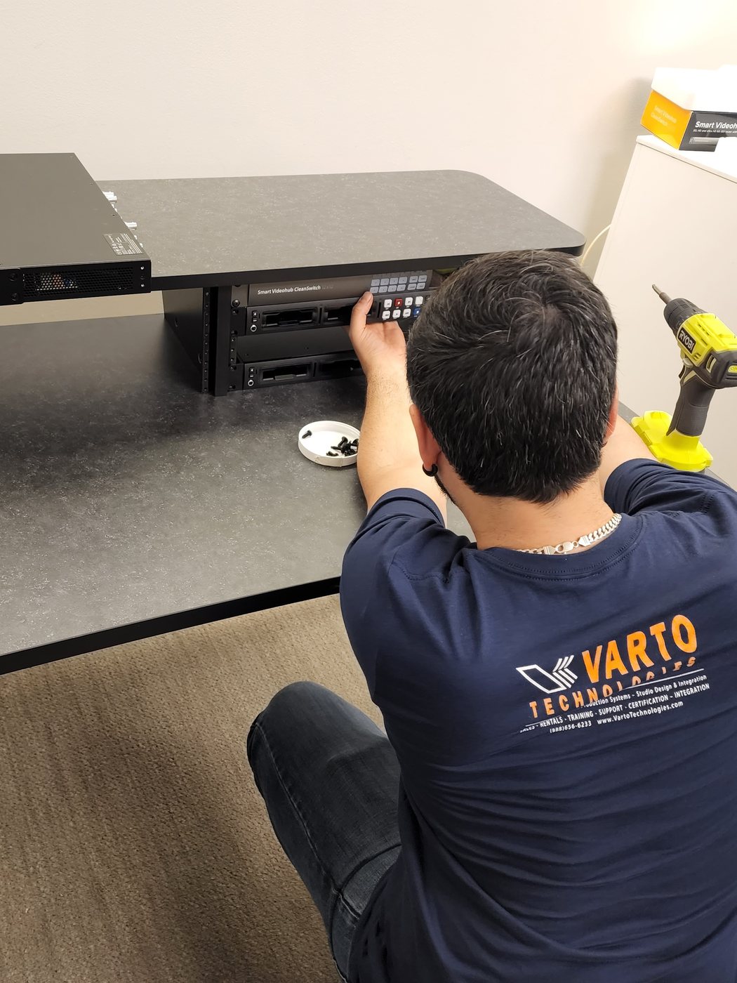 Varto technician, seen from behind, fitting a video router into a production desk