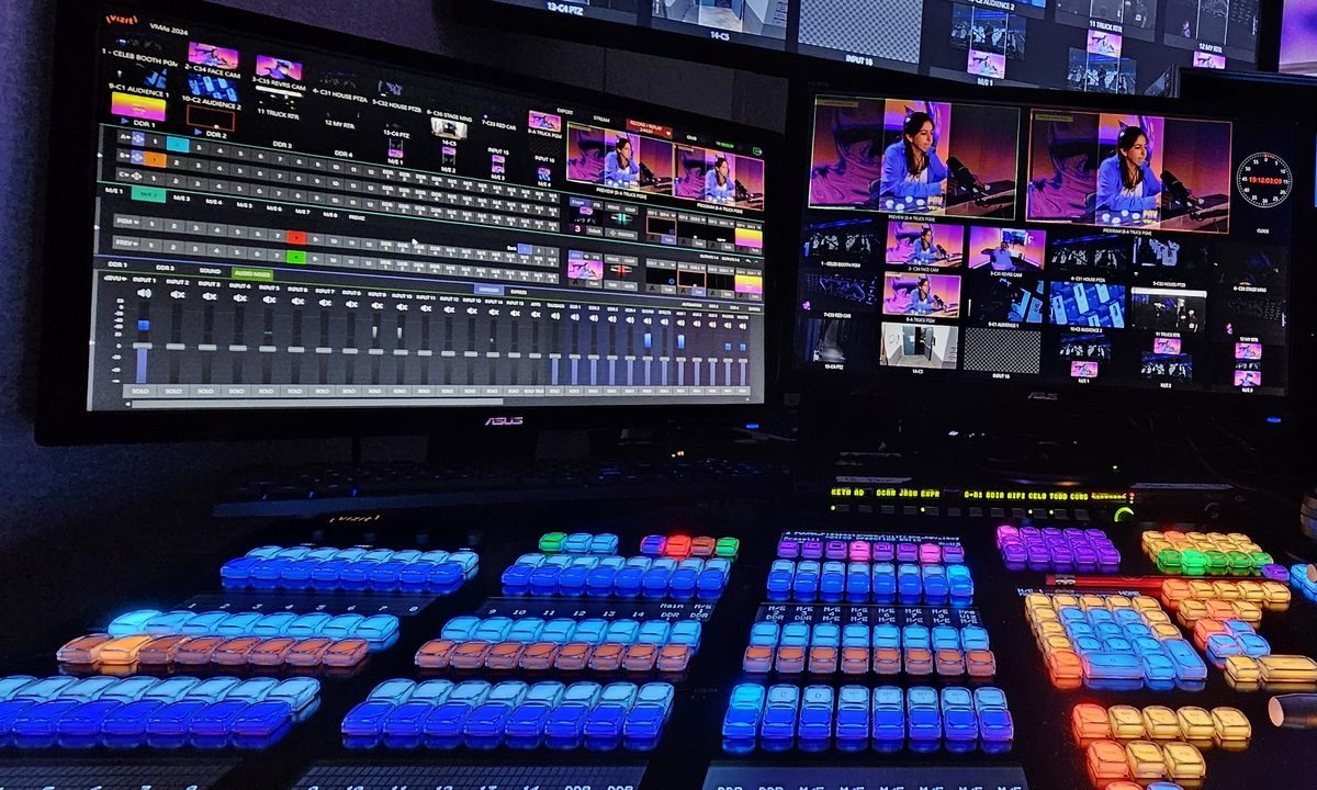 A lit TriCaster control surface under a wall of production monitors during a live show