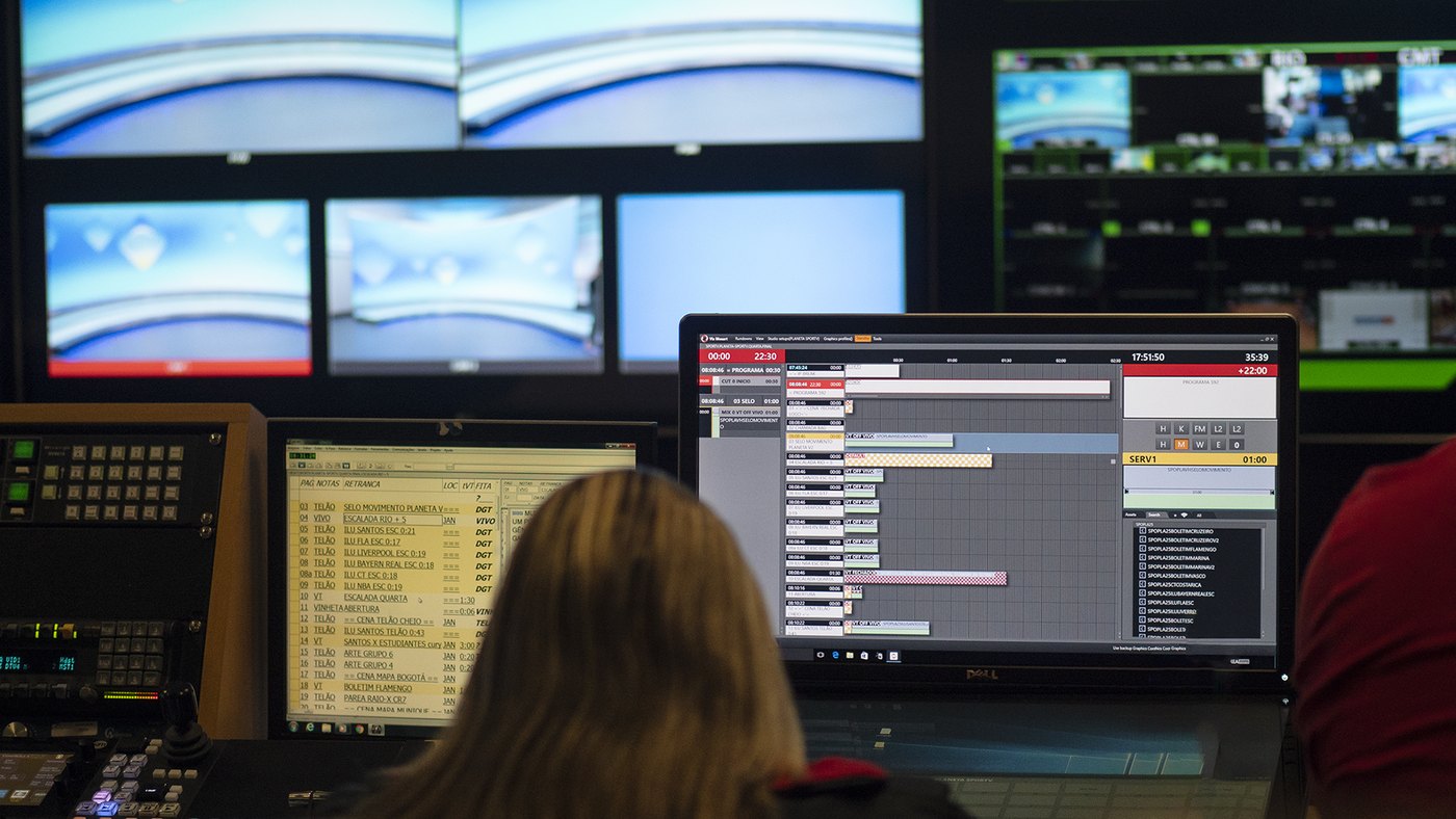 An operator at a Viz Mosart screen in a broadcast control room, the rundown on the monitor and a wall of preview monitors above