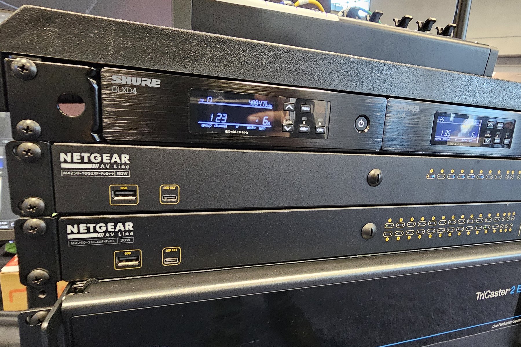 Two Shure QLXD4 wireless receivers racked above NETGEAR AV switches and a TriCaster 2 Elite