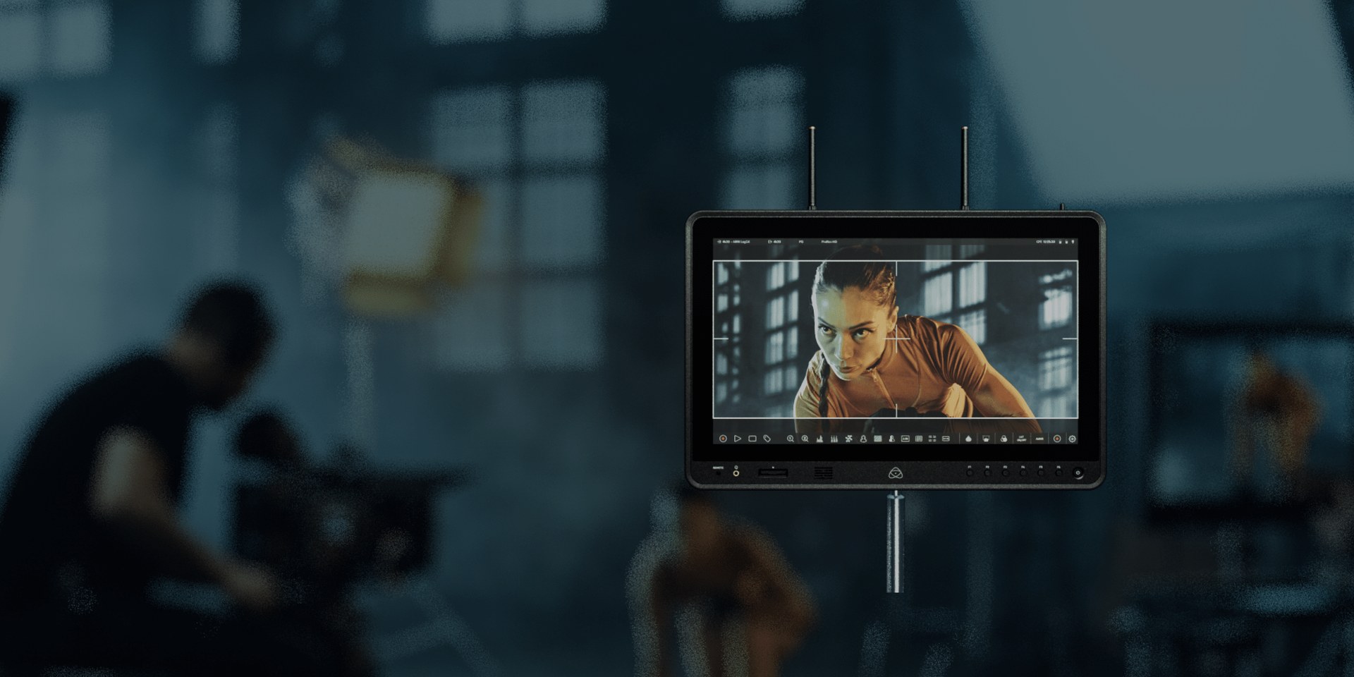 An Atomos Sumo PRO-19 monitor-recorder on a stand in front of a blurred film set, showing a framed shot of an athlete