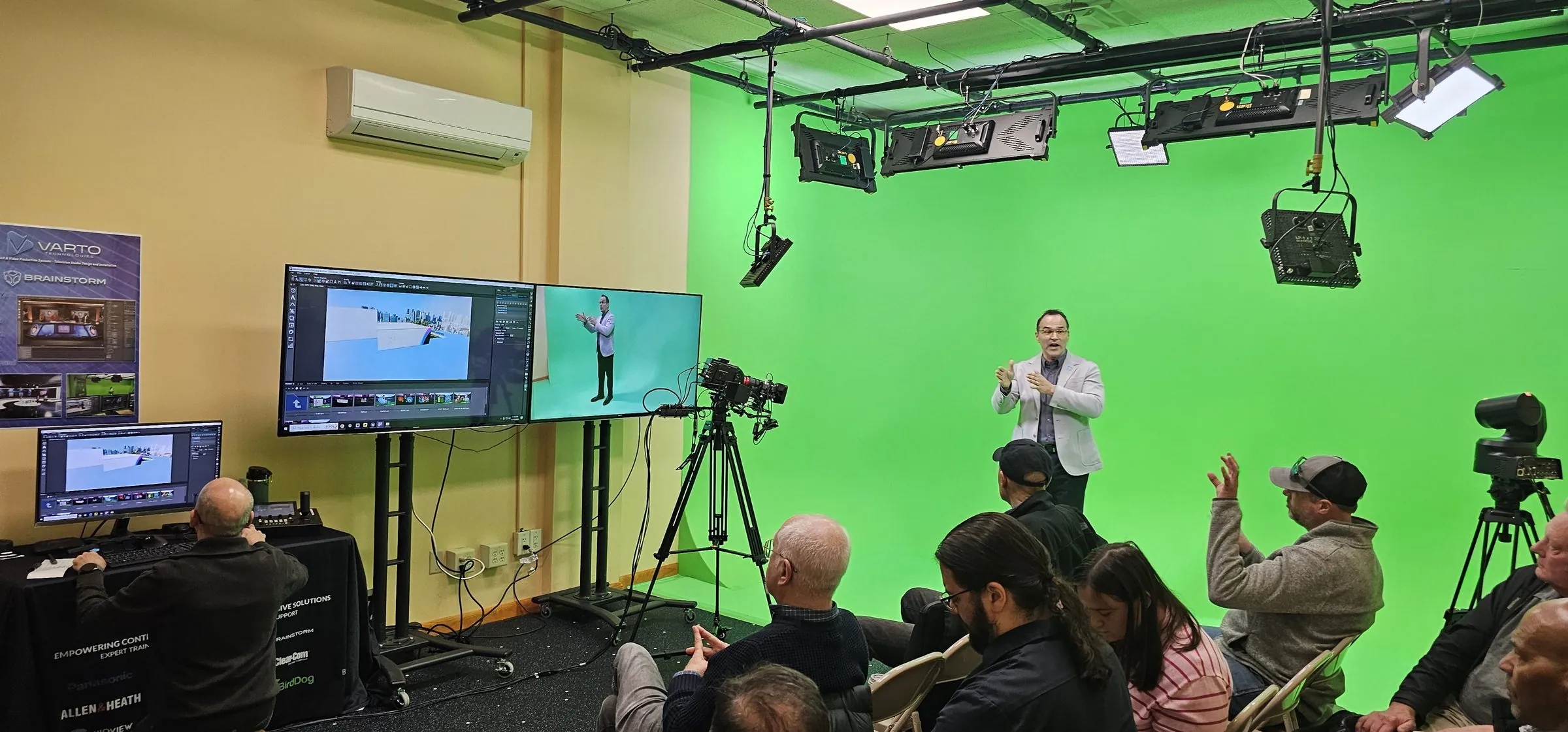A presenter on a green cyclorama while monitors show the virtual set and the keyed shot, with an audience watching