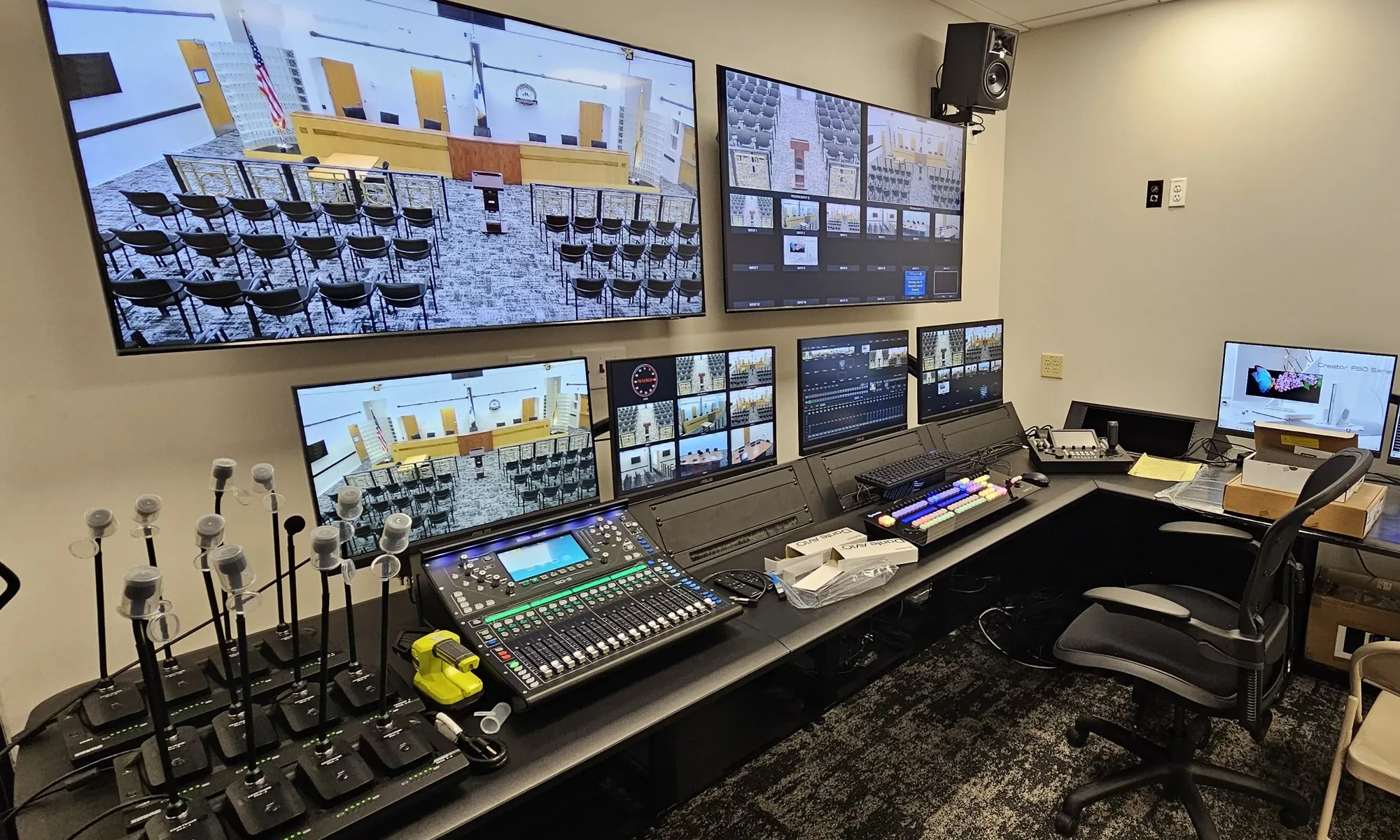 Township control room with wall monitors carrying council chamber feeds, an audio console and gooseneck microphones