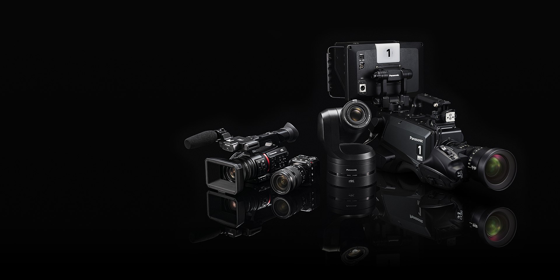 Panasonic cameras on a dark floor with reflections: a handheld camcorder, a compact box camera, a black PTZ camera and a studio camera with a viewfinder