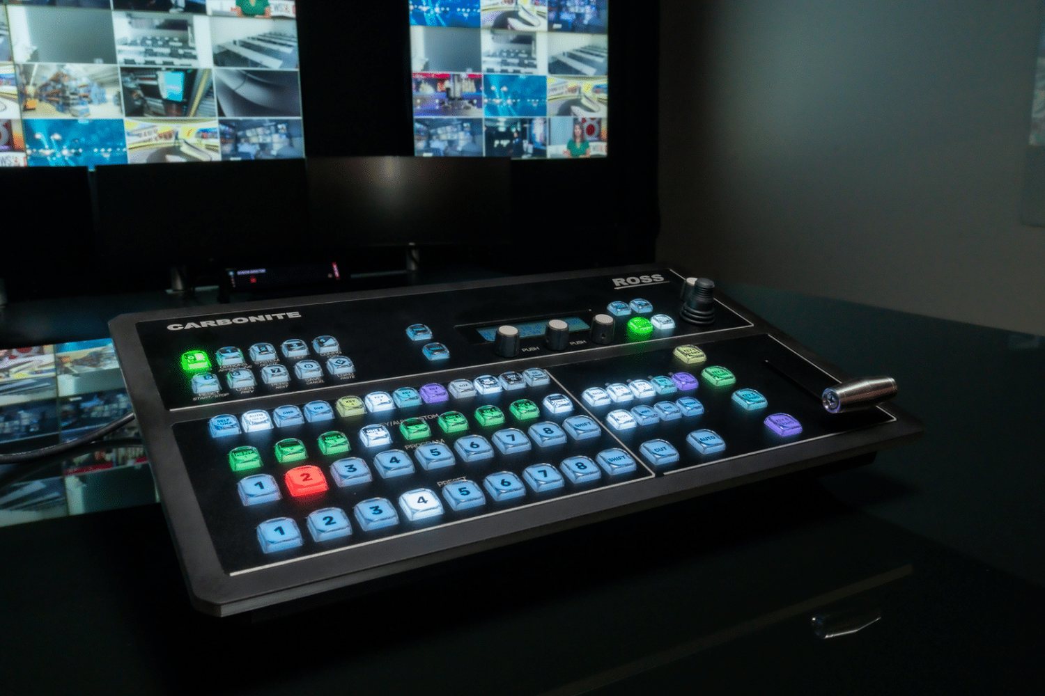 A Carbonite Ultra Solo control panel on a desk in front of a softly lit monitor wall