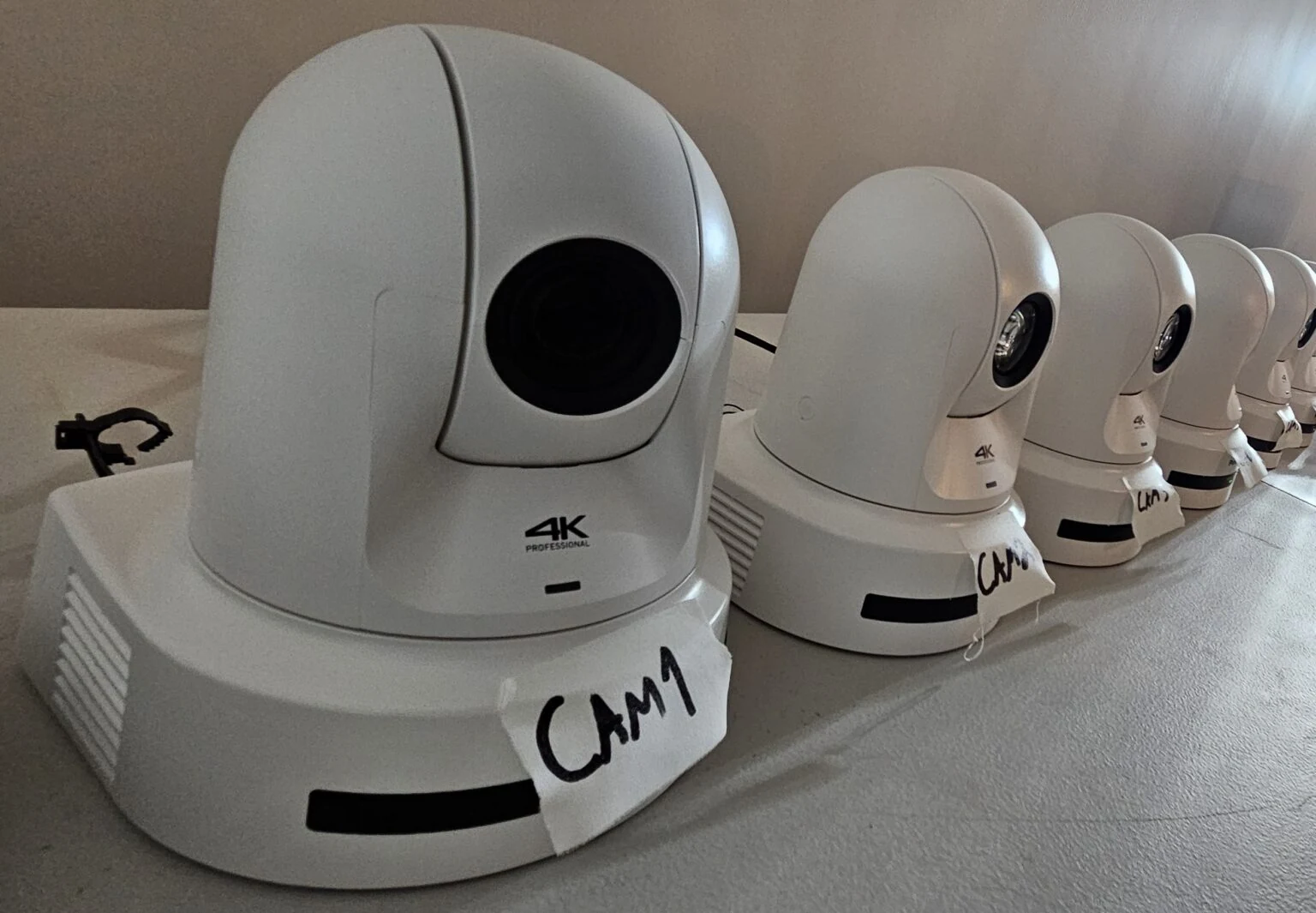 Six white PTZ cameras lined up on a work table, the nearest with a hand-written CAM 1 label on its base